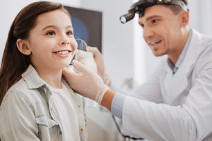 A medical professional wearing medical head gear and examining the ear of a young girl