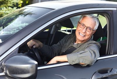 Older man smiling and hanging his arm out the window of a car
