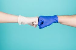 This is a picture of two hands fist bumping, one wearing white gloves and the other wearing a blue glove.
