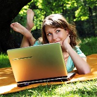 A photo of a woman sitting on a blanket at a picnic looking at her laptop