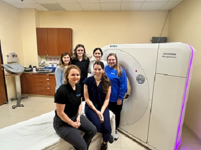 A group of medical professionals standing in front of a large medical machine posing for a photo