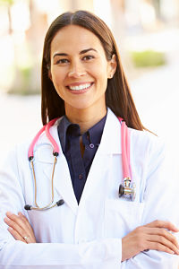 A smiling woman wearing a white lab coat and a pink stethoscope around her neck
