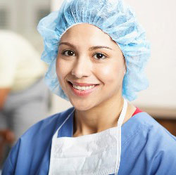 A smiling photo of a female doctor wearing a medical hair net and a medical face mask hanging around her neck