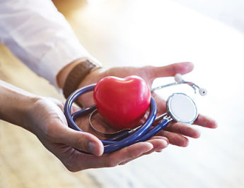 Photo of a pair of hands holding a plastic red heart and a stethoscope