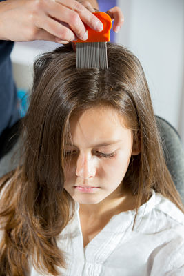 A little girl looking down while someone combs through her hair to check for lice