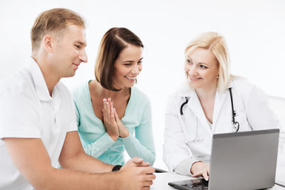 A female doctor sitting next to a man and woman showing them something on a laptop