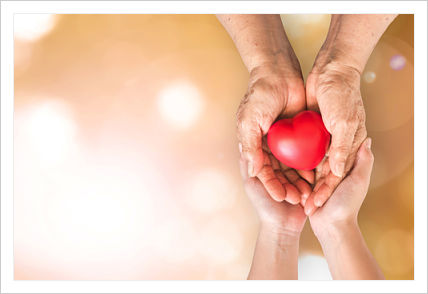 A pair of hands holding another pair of hands that are holding a plastic red heart