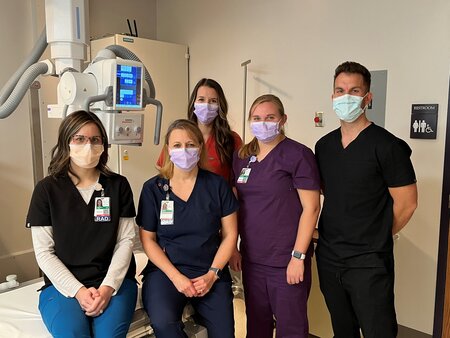 A group of medical professionals standing in front of a large medical machine posing for a photo