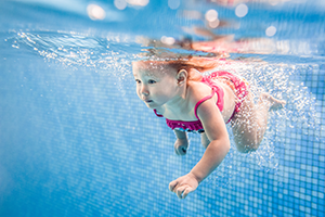 A group of children wearing goggles and swimming caps swimming in a pool