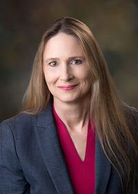 Picture of Leah Buthorne, APRN (Dermatology), wearing a dark pink shirt under a gray suit coat.