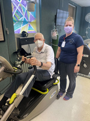 Male patient exercising using Cardiac Rehabilitation machine as a female medical staff member monitors him.