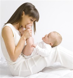 A woman wearing all white sitting on the ground holding a baby in her lap