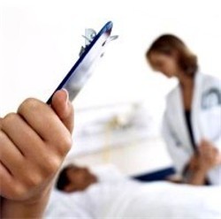 A person holding a clipboard with the blurred image of a female doctor tending to a patient laying in bed